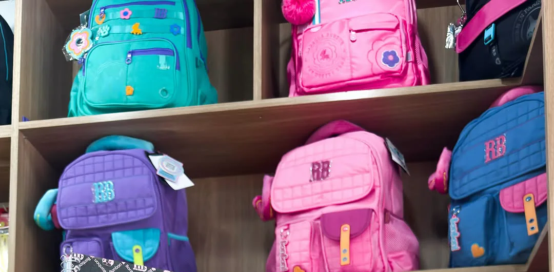 Prateleira de madeira cheia de mochilas Rebecca Bonbon em verde-água, roxo, rosa, pink e azul